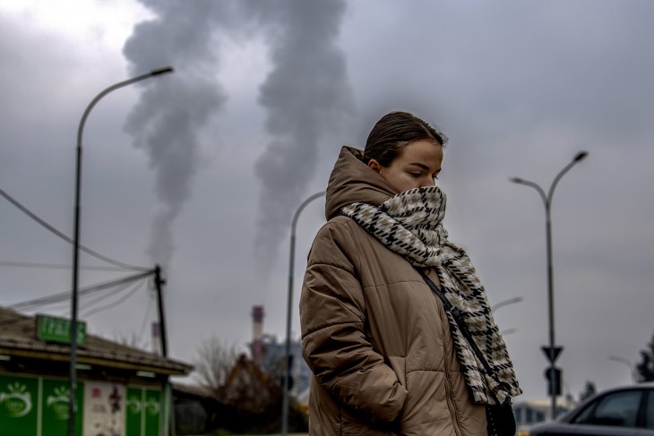 Az arcát sállal eltakaró nő megy füstölgő gyárkéményekkel a háttérben Szkopjéban 2022. december 30-án. A klnikák és kórházak nem győzik ellátni a légúti megbetegedéssel küzdő lakosokat. Az IQAir svájci levegőminőségi technológiai vállalat egy héttel ezelőtt nevezte meg Szkopjét a világ harmadik legszennyezettebb levegőjű városának. Fotó: MTI/EPA/Georgi Licovszki 