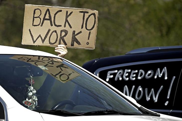 Vissza a munkába! feliratú plakátot tart a kezében egy autóban ülő tüntető a koronavírus-járvány miatt bevezetett korlátozó intézkedések elleni tüntetésen Kansas állam parlamentje előtt 2020. április 23-án. (Fotó: MTI/AP/Charlie Riedel)