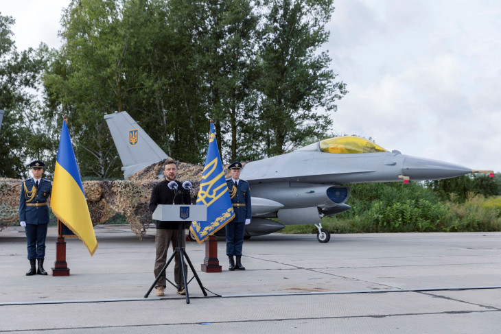 Volodimir Zelenszkij sajtótájékoztatót tart, mögötte egy frissen érkezett F-16-os