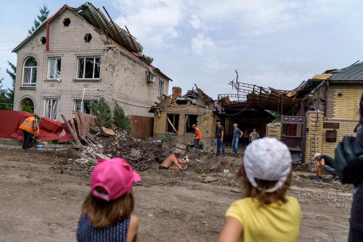 Egy kramatorszki bombatölcsér körüli helyreállítási munkát nézik gyermekek, miután orosz rakétatámadás érte a Donyecki területen fekvő várost. Fotó: MTI/AP