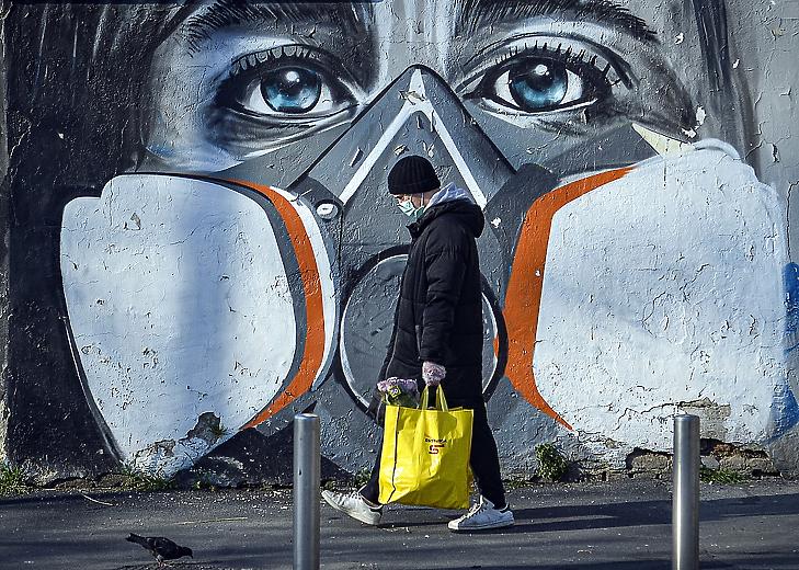 Védőmaszkos embert ábrázoló falfestmény előtt egy járókelő Milánóban 2020. március 16-án. MTI/EPA/ANSA/Andrea Fasani
