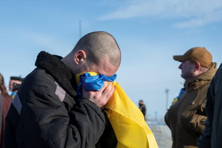 Az orosz hadifogságból hazatérő ukrán katona a hazája lobogójába temeti arcát. Fotó: MTI/EPA/Ukrán elnöki sajtószolgálat