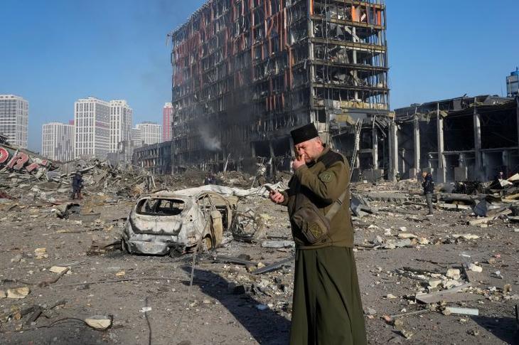 Tüzérségi támadásban megsemmisült bevásárlóközpont romjainál imádkozik egy pap Kijevben 2022. március 21-én.  Fotó: MTI/AP