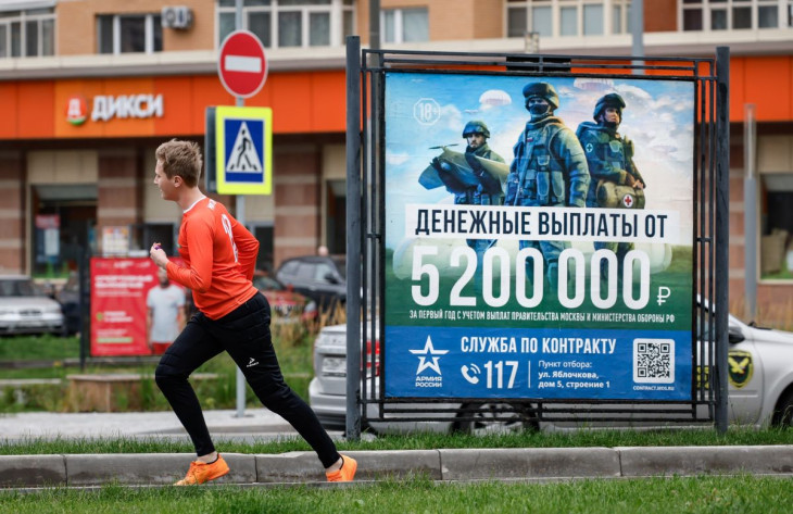 Férfi fut egy orosz katonákat ábrázoló toborzóplakát előtt Moszkvában az Ukrajna elleni orosz háború alatt, 2024. augusztus 20-án. A poszteren 5 200 000 rubel fizetést ígérnek egy év szolgálatért